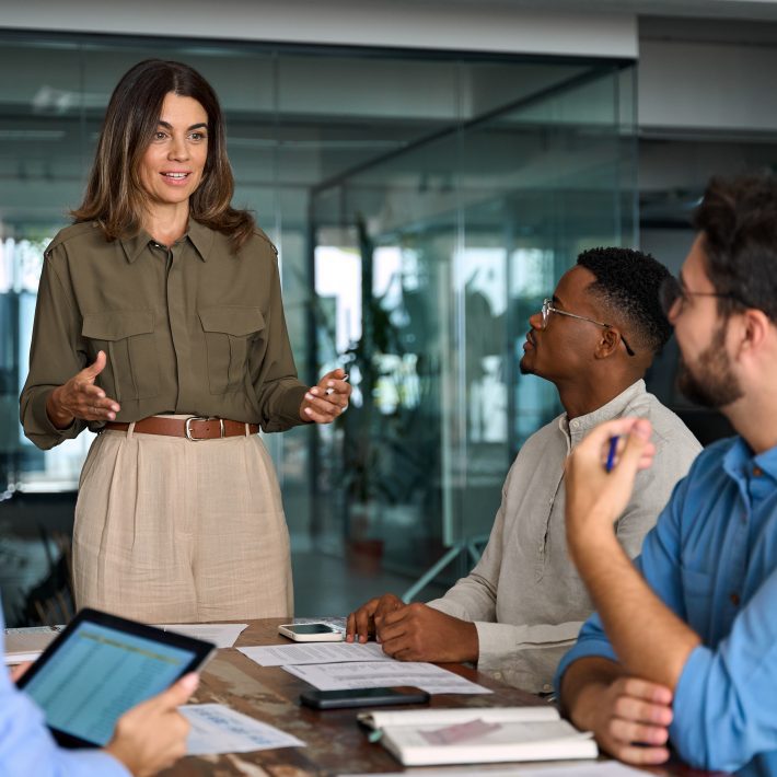 Happy middle aged business woman leader working with diverse team at meeting.
