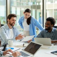 Various business teams collaborating on a project using laptops and documents in a modern office