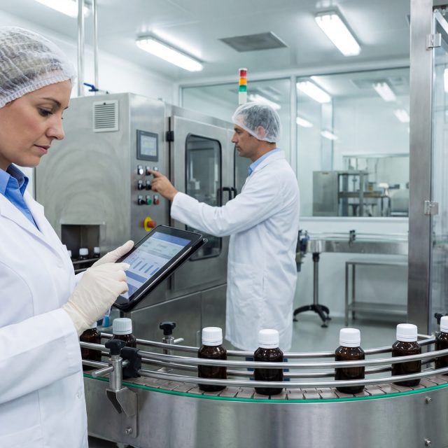 Pharmaceutical manufacturing professionals working on production line with tablet and machinery